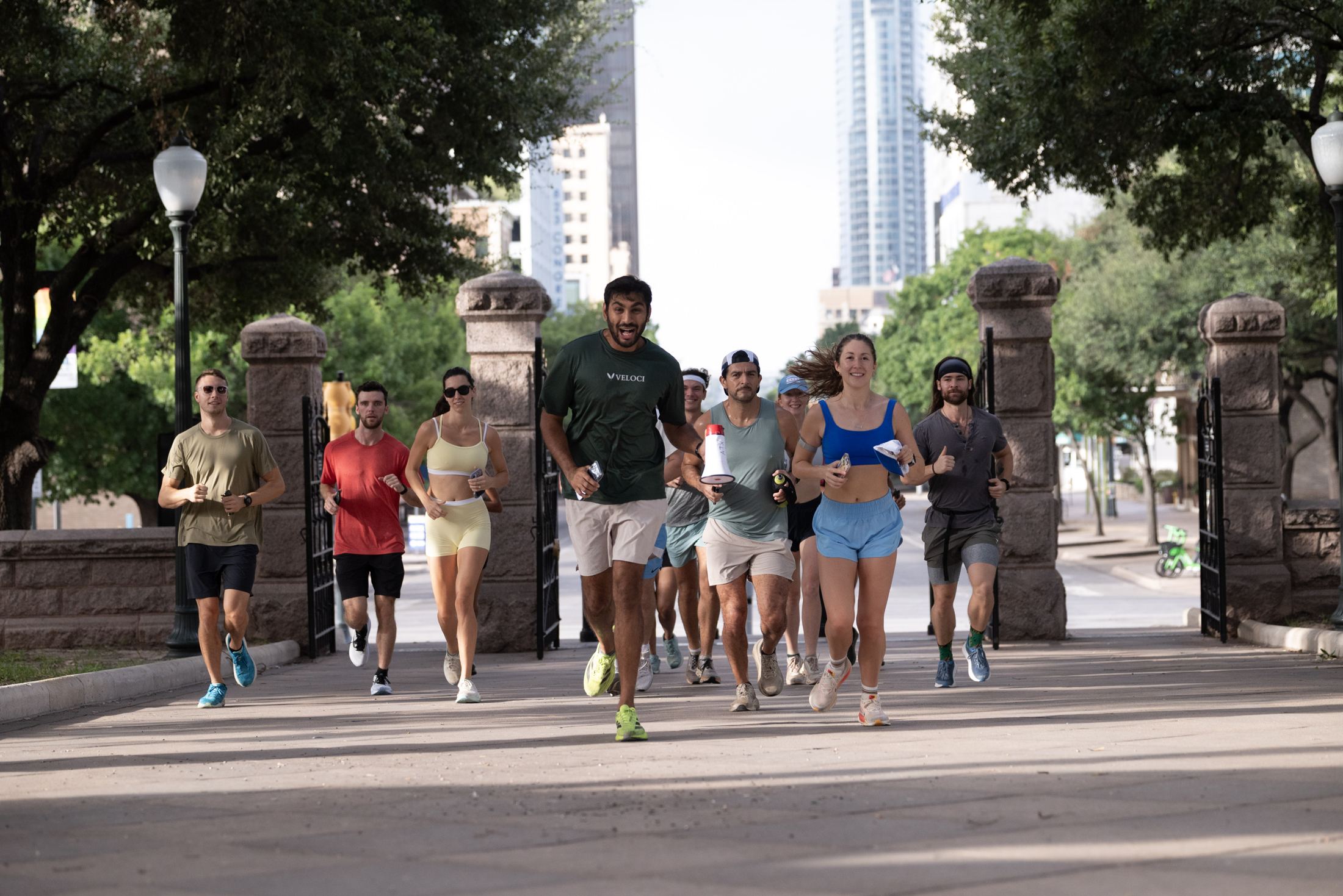 A group of runners on an ATX Run Tours pilot run, jogging through the gates of the Texas Capitol grounds with the downtown skyline behind them